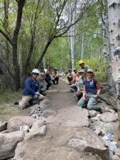 Trail work An image of a group of workers are crouched down on either side of a trail.